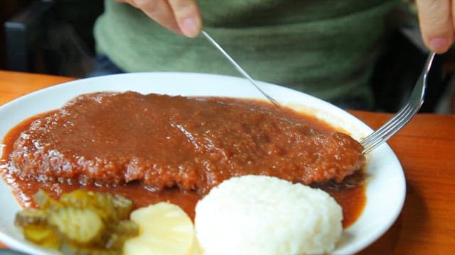 Person cutting a saucy pork cutlet