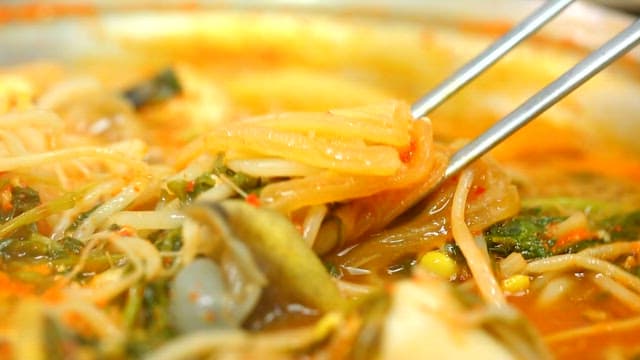 Chopsticks holding kimchi and vegetables in stew