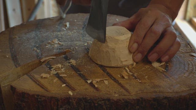 Hands carving wood with an axe