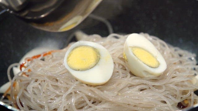 Pouring the broth into the pan with the boiled eggs and glass noodles