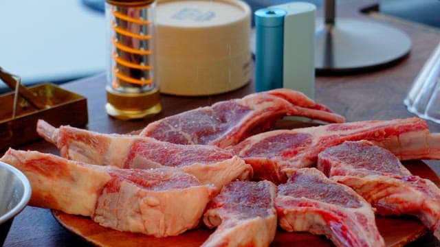 Seasoning fresh lamb chops with salt on a wooden board