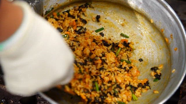Mixing Korean fried rice with seaweed and vegetables using wooden spatula