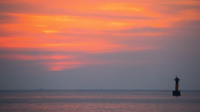 Sunset over the ocean with a lighthouse in the distance