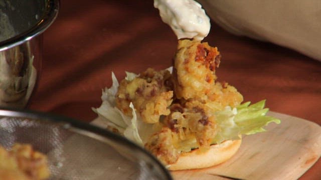 Sauce being added to a burger with crispy fried pork