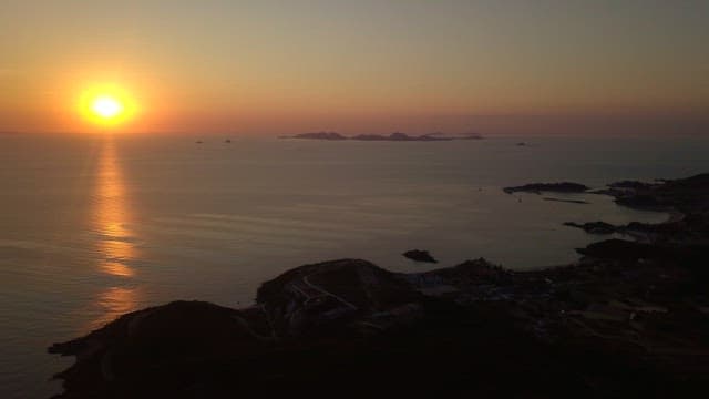 Sunset over a calm sea with distant islands and coastal buildings