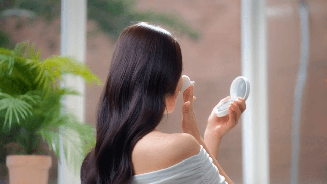 Woman in white top applying makeup with a mirror of cushion foundation