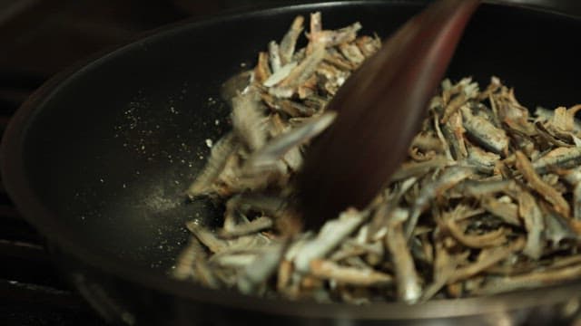 Stirring dried fish in a frying pan