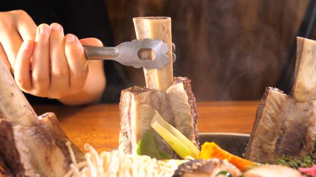 Taking out ribs from a steaming hot Galbitang with tongs