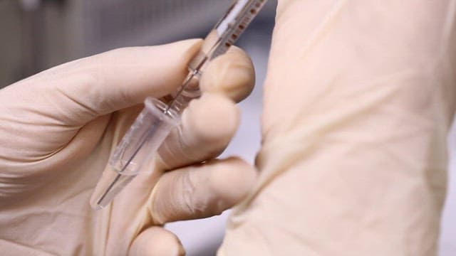 Gloved handextracting an experimental solution with a syringe