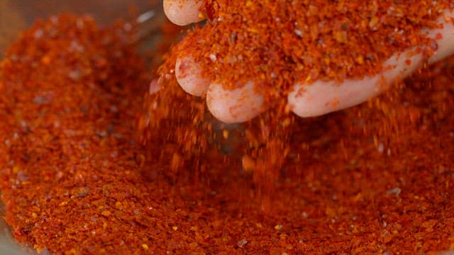 Red chili flakes being poured by hand