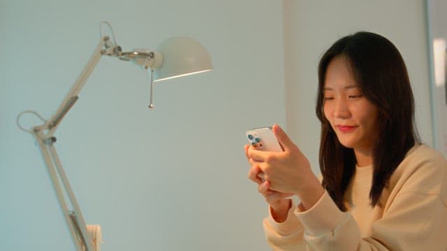 Woman using a smartphone at a desk in a calmly lit room