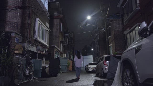 Woman walking alone in a residential alley with street lights on at night