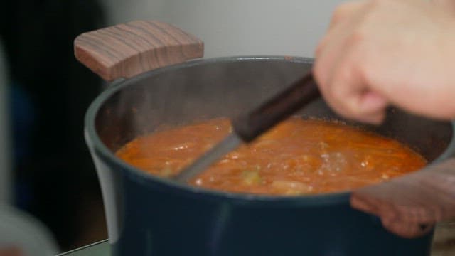 Scooping up boiling zucchini kimchi stew in a pot with ladle