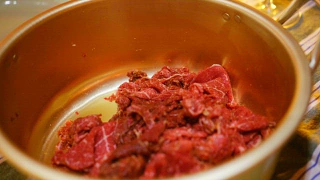 Gloved hands mixing meat and seasoning in a nickel-silver pot