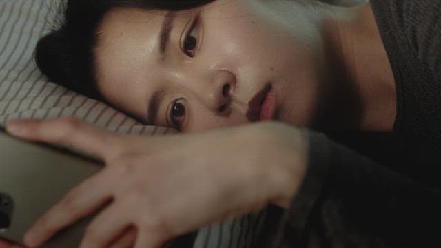 Woman lying in bed, looking at her phone