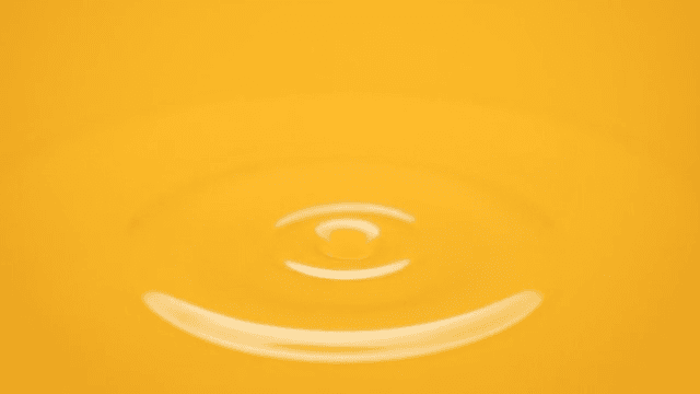 Drop of water forming ripples on a yellow liquid surface