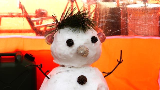 Snowman made with pin cones and seashells next to an orange tent