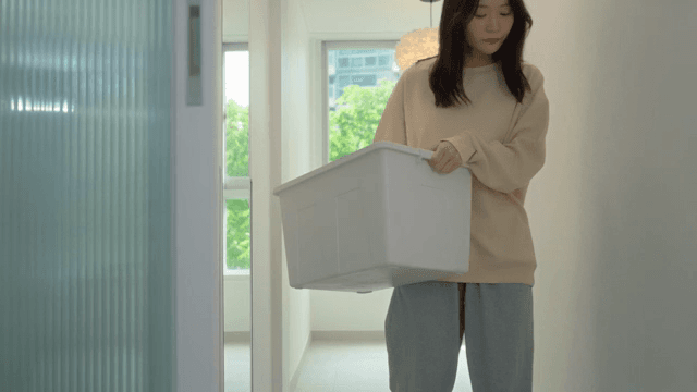 Woman walking through house with bright interior holding storage box