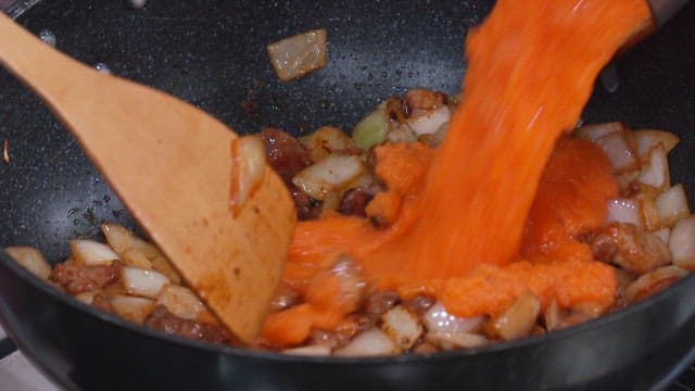 Pouring Carrot Juice into a Pan with Onions and Meat