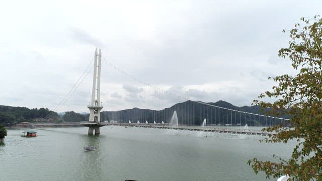 A long bridge with water fountains over the river on a cloudy day