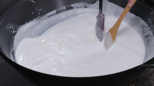 Mixing of thick white batter in a large bowl using wooden spatulas