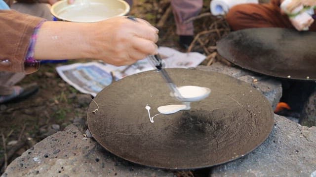 Thin layer of flour dough spread with a ladle on an outdoor griddle