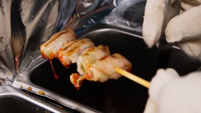 Gloved hands brushing sauce to grilled skewers in the kitchen