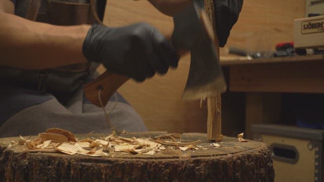 Person carving wood with an axe indoors