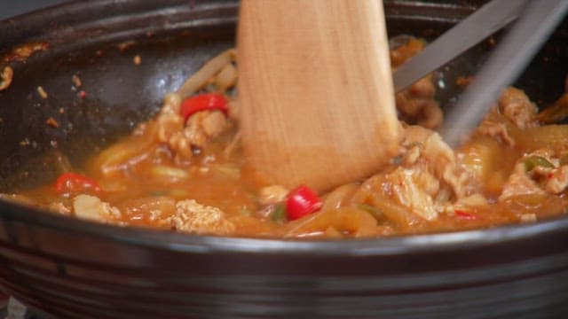 Stirring the remaining food in the pan with a wooden spatula and scissors
