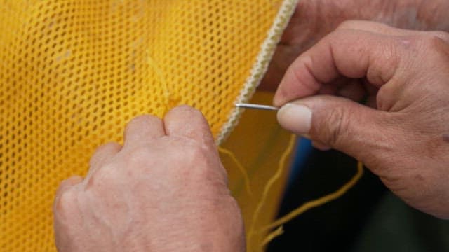Hands of an elderly person sewing a yellow fabric of fishing net