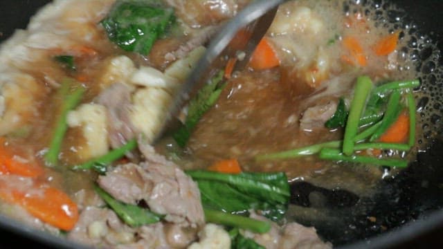 Pouring soy sauce into a pan and stir-frying vegetables and meat