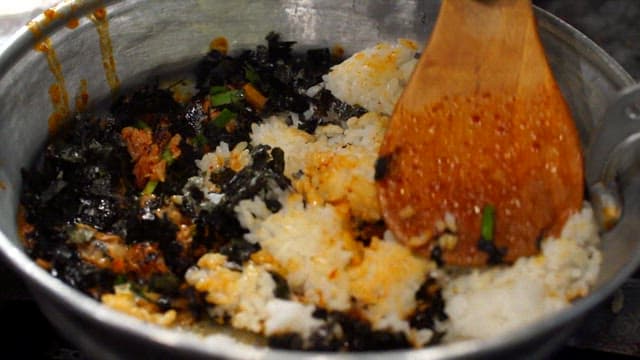 Mixing Korean fried rice with seaweed and vegetables using wooden spatula
