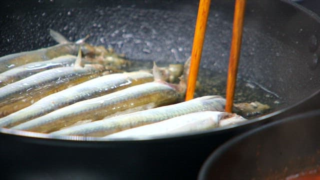 Grilling sand eels with chopsticks in an oiled pan