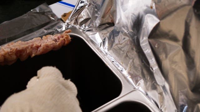 Gloved hands brushing sauce to grilled skewers in the kitchen