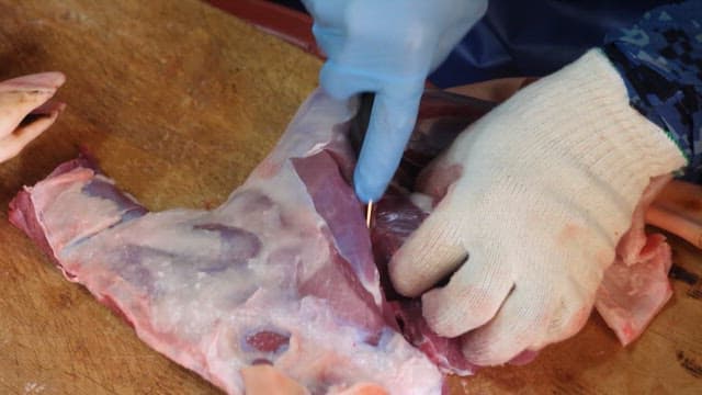 Cutting raw meat on a wooden board with gloves on