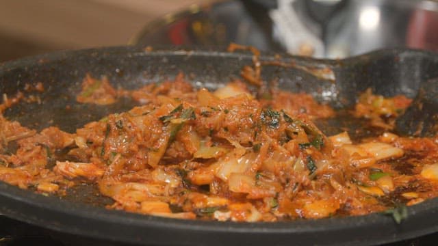 Cooking kimchi fried rice in a hot pan on a stove with wooden spatula