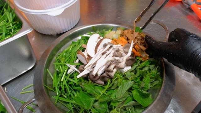 Fresh greens and mushrooms in a metal bowl for hotpot dish