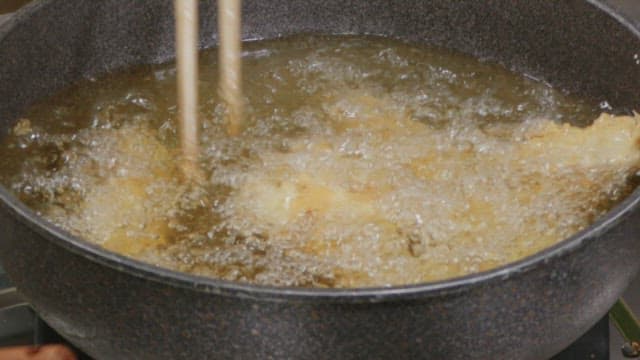 Frying tempura in a boiling oil pan with chopsticks