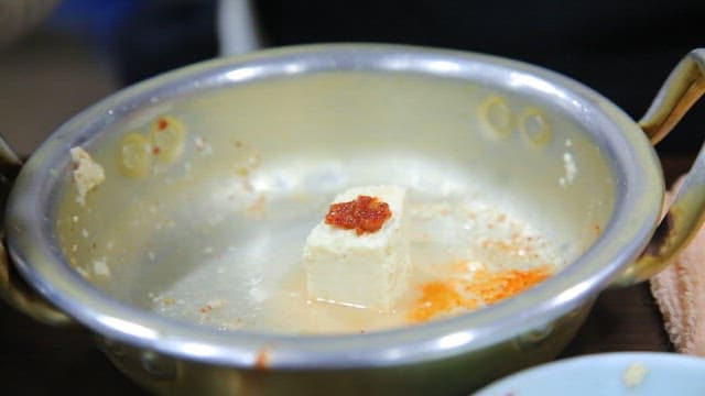 Seasoning sauce being poured over tofu in a pot with chopsticks