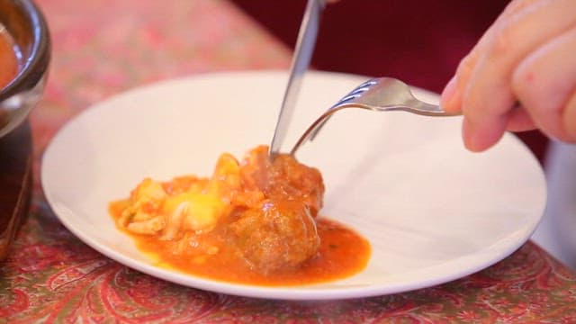 Knife cutting beef kofta with warm sauce