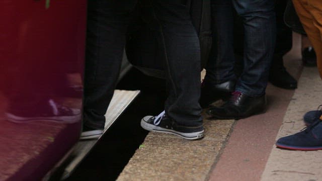 Legs of people boarding a train at a busy station platform