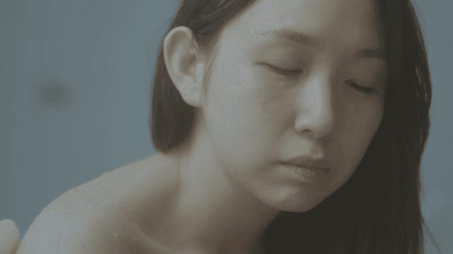 Woman in a bathroom, appears contemplative and slightly melancholic.