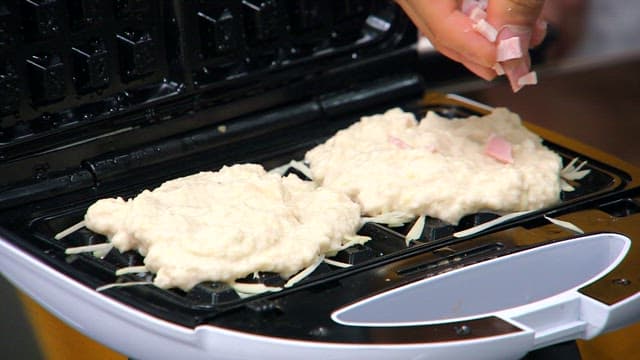 Topping potato batter with chopped bacon on waffle maker