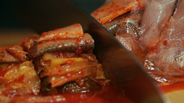 Kimchi with large-eyed herring being sliced ​​on a wooden cutting board
