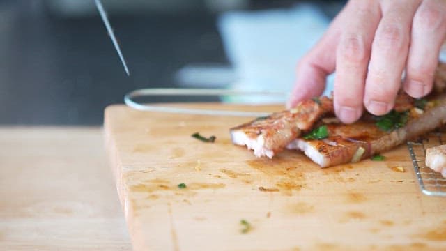 Cutting grilled pork belly on a wooden cutting board in the kitchen
