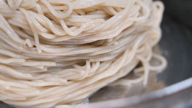 Preparing cold noodles by adding garnish and pouring broth