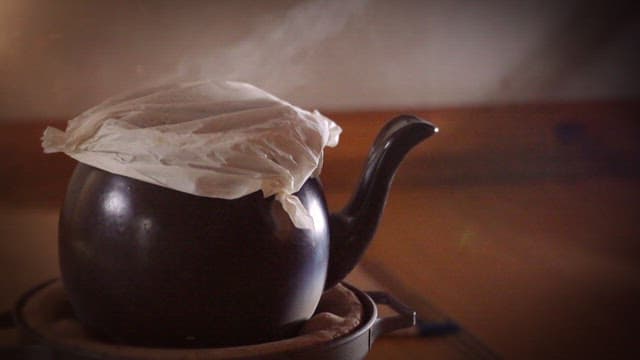 Steam rising from a covered traditional teapot in a cozy kitchen