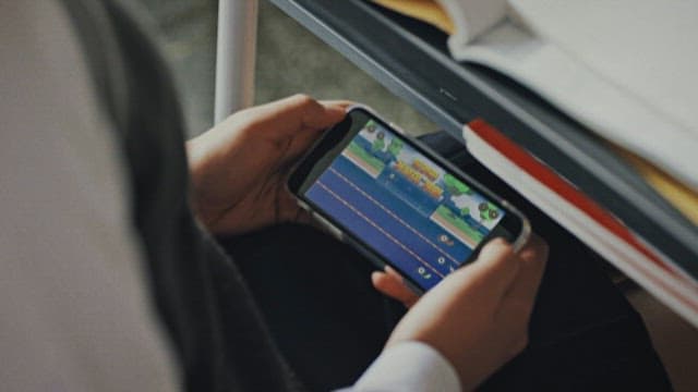 Person Playing Mobile Games on Cell Phone Under Desk