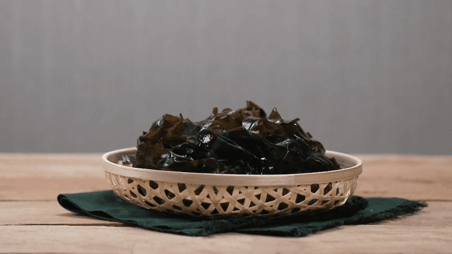 Basket of fresh seaweed on a wooden table.