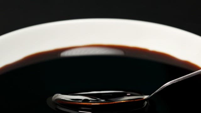 Pouring of dark chocolate syrup into a white bowl with a spoon